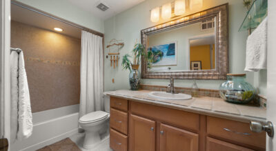 Located at 8725 E San Marino Dr in McCormick Ranch, this bathroom features a beige countertop, wooden cabinets, a large mirror, and a bathtub with a shower curtain. Plants and decorative items adorn the counter, enhancing its welcoming ambiance.