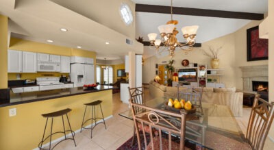 Located at 8725 E San Marino Dr in McCormick Ranch, this open-concept kitchen and living room features yellow walls, white cabinets, a chandelier, and a glass dining table with pears. Relax by the cozy seating area near the fireplace or enjoy your meal on one of the two bar stools.